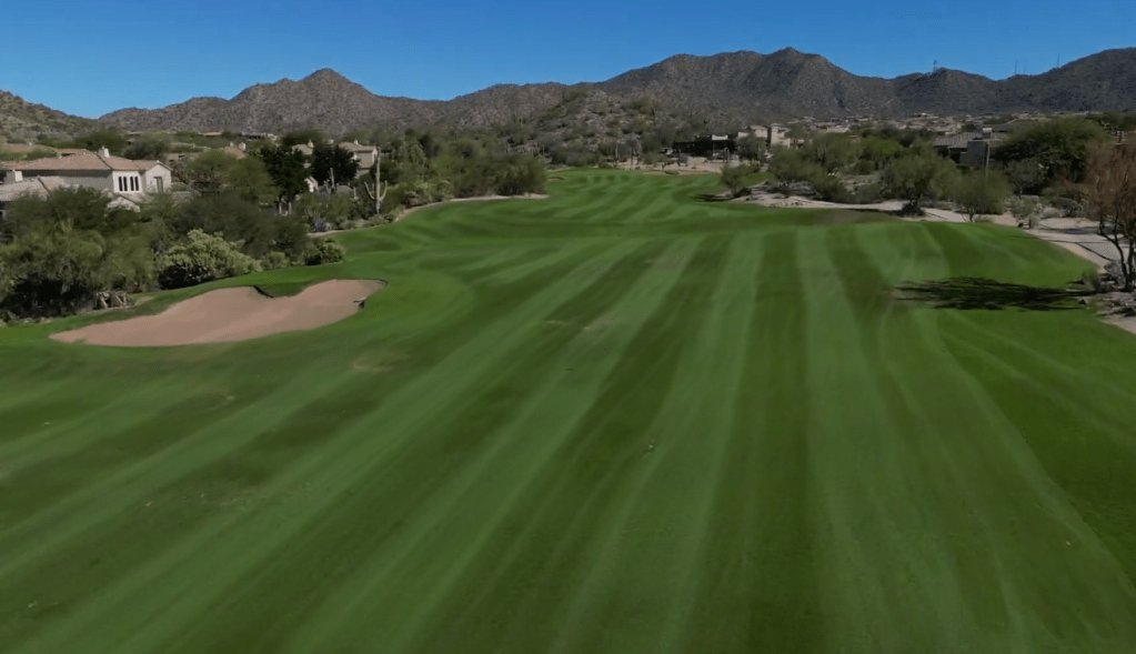 Freshly manicured golf fairway stretching toward surrounding hills under a clear sky.